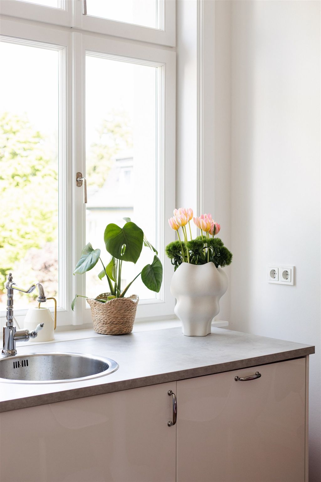 Eine Küchenarbeitsplatte mit zwei Topfpflanzen und einem Fenster mit Blick auf das Grün draußen.