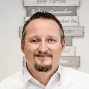 A friendly man with short dark hair and a goatee, wearing a white shirt, smiling at the camera.