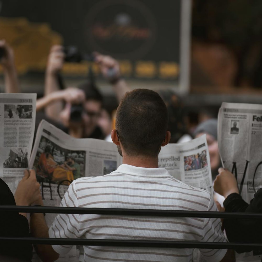 Three people read newspapers on a park bench in Ankara, Türkiye