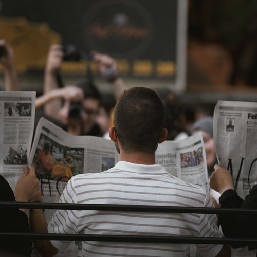 Three people read newspapers on a park bench in Ankara, Türkiye