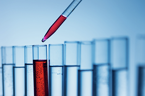 Laboraufnahme von Reagenzgläsern, in die mit einer Pipette eine rote Lösung zur Inhaltsstoff-Analyse getropft wird.