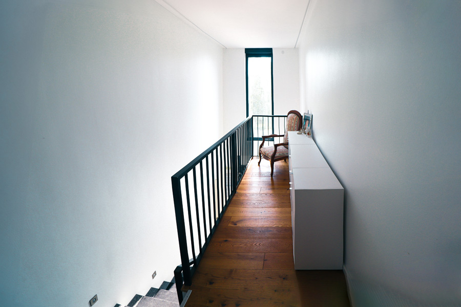 Galerie im Obergeschoss mit Holzdielenboden, schwarzem Treppengeländer, langem weißem Sideboard und bodentiefem Fenster.