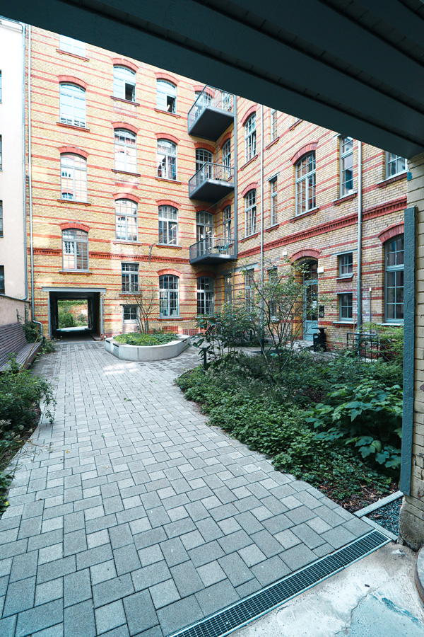 Blick in den begrünten Innenhof mit gelb-roter Klinkerfassade und Balkonen, mit neu verlegtem Pflasterbelag und rundem Pflanzbeet im Vordergrund.