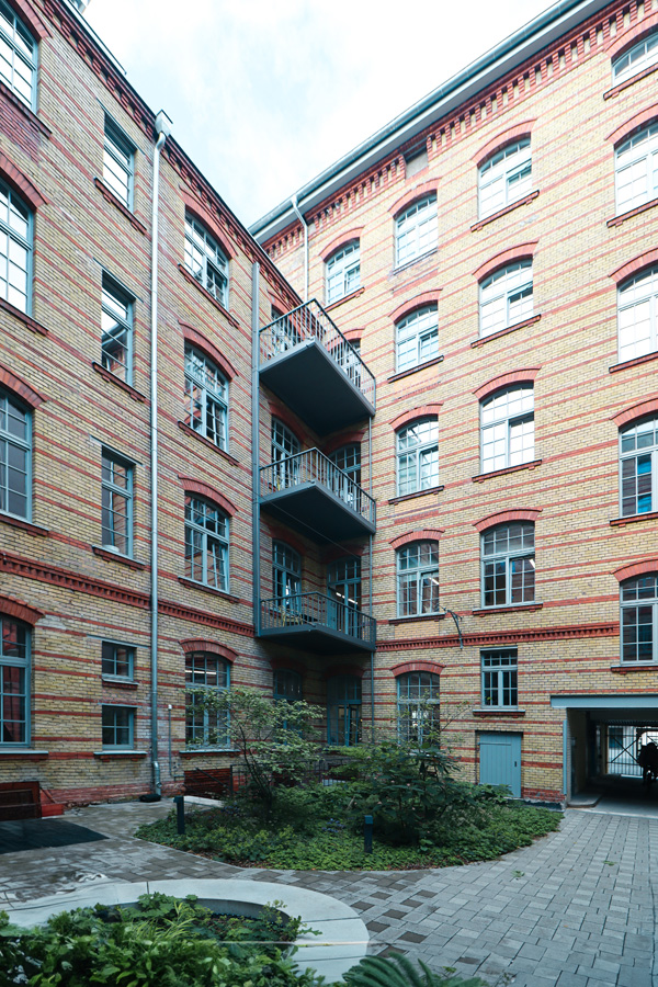 Eckansicht des Innenhofs mit gelb-roter Klinkerfassade und vorgesetztem Stahl-Balkonturm zwischen zwei Gebäudeflügeln.