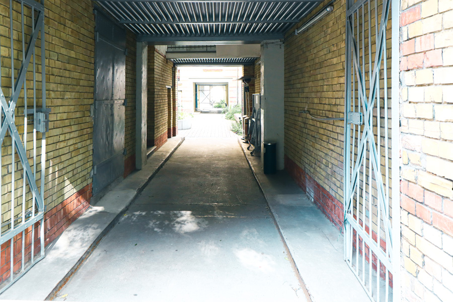 Tordurchfahrt mit Wellblech-Stahldecke und gelb glasierten Klinkerwänden, geöffnete Toranlage mit Durchblick in den Hof.
