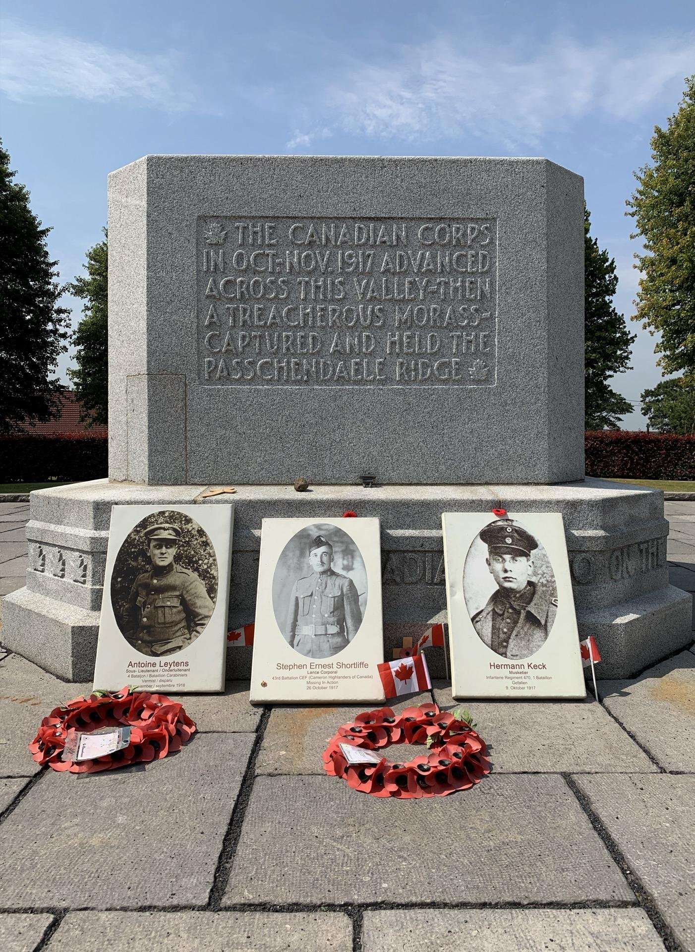 This image shows a war memorial dedicated to the Canadian Corps, indicating their military effort in October and November 1917 during World War I. The inscription on the monument marks their advancement across a valley, describing it as a treacherous morass, and their capture and holding of Passchendaele Ridge.

In front of the monument, there are three portraits placed on the base, each with a name beneath them: Antoine Leytens, Stephen Ernest Shortliffe, and Hermann Keck. These likely represent soldiers who participated in the historical events commemorated by the memorial. Below the portraits, there are wreaths adorned with red poppies, a symbol often used to remember those who have died in military service, particularly in British and Commonwealth countries. Small Canadian flags are also placed near the portraits, emphasizing the memorial’s connection to Canada and its historical military contributions.