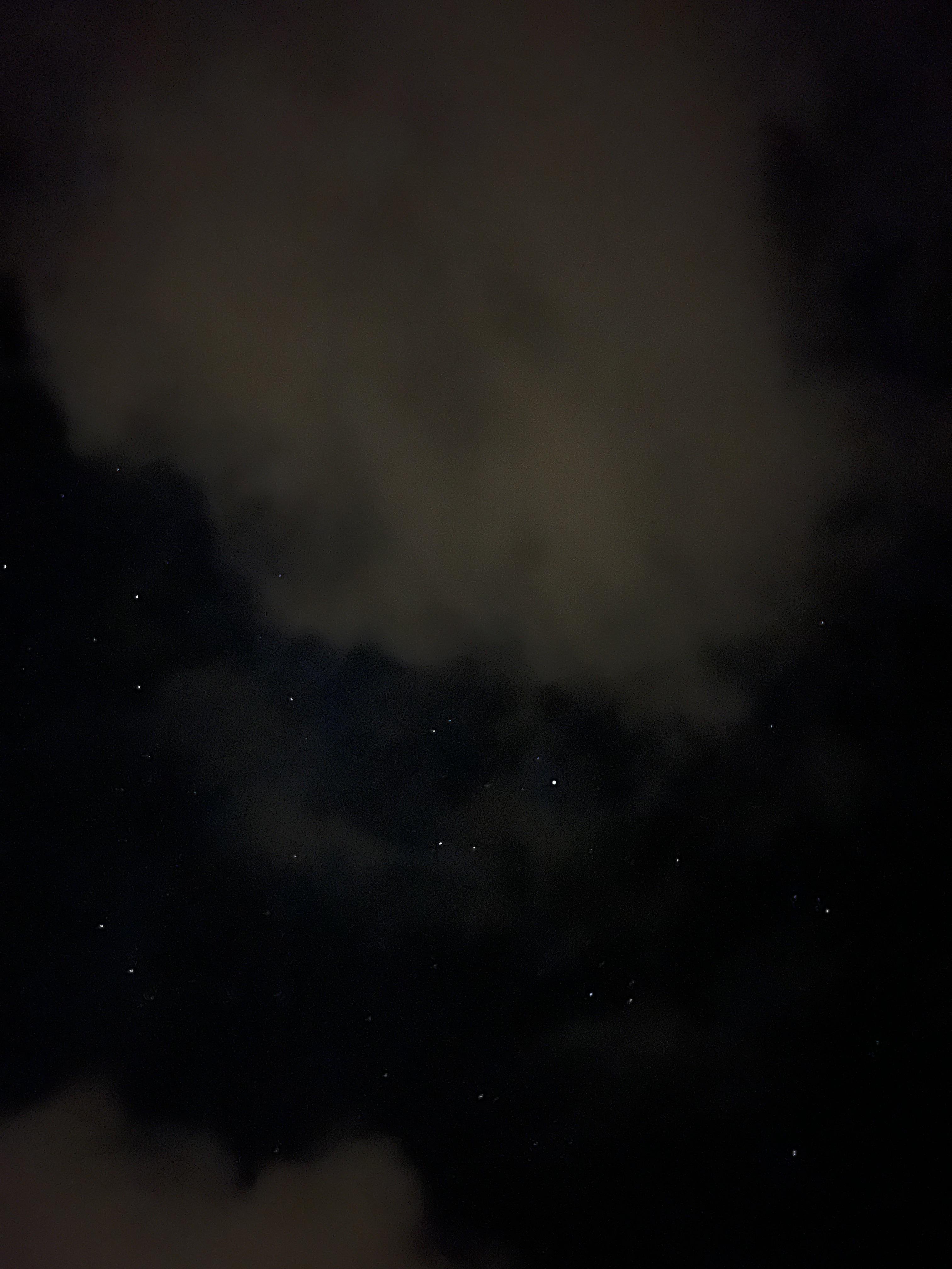 Night sky with visible star constellations amidst clouds. The image is predominantly dark with subtle cloud patterns and scattered bright stars visible against the black background.